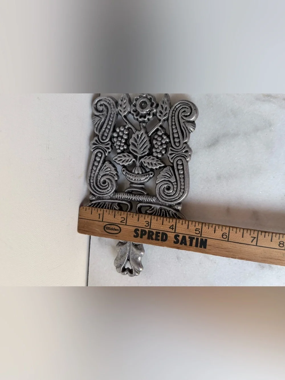 vintage silver-toned metal trivet featuring a decorative design grapes scrolls.